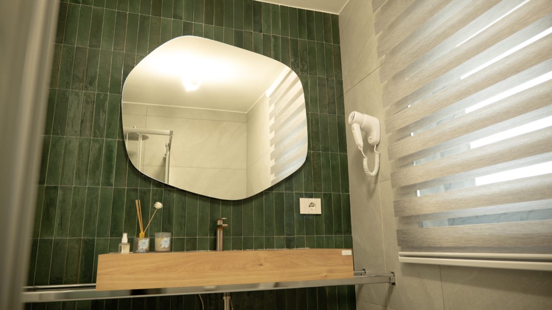 Bagno rivestito in verde con specchio tondo, mobile in legno e tenda a righe