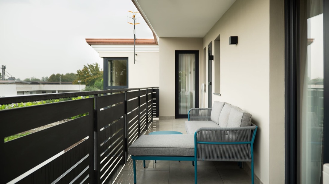 Balcone con divano in corda grigia, tavolino teal e vista sulla campagna