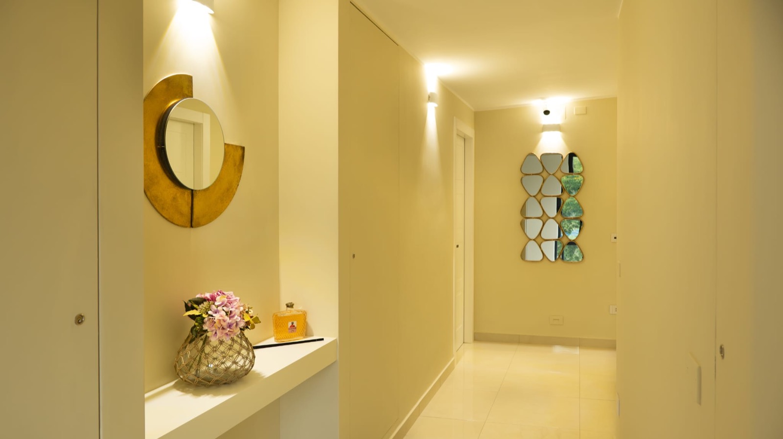 Ingresso di Domino Suite House con specchio tondo dorato, fiori e luce calda